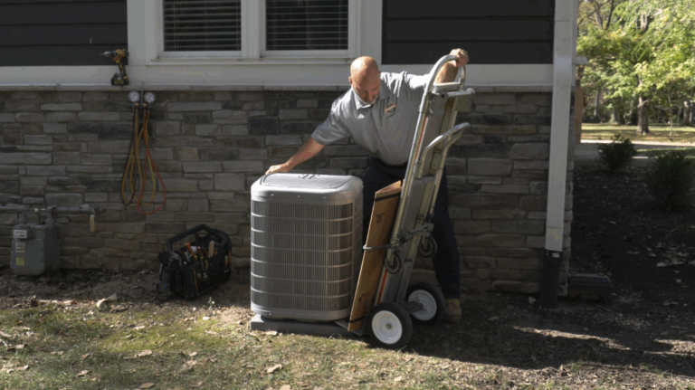 An HVAC Contractor from Brown Cooling and Plumbing provides AC installation in Palmetto, FL outside a customer's home, unloading a condenser off a moving dolly